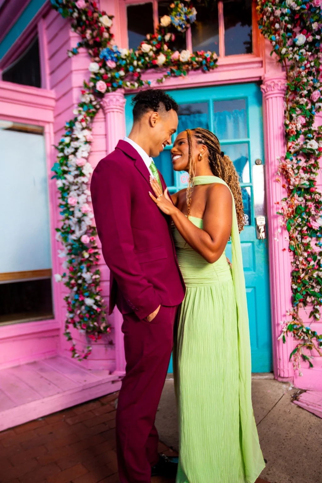 Alexis and Gary smiling in front of a floral-covered pink building